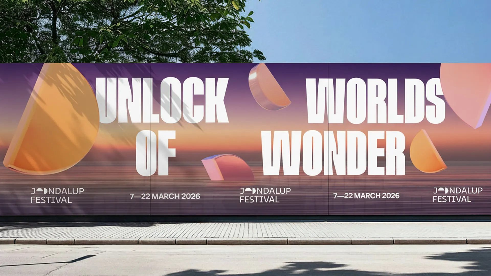 Large-format street hoarding for Joondalup Festival 2026 showing Unlock Worlds of Wonder headline with prismatic 3D hemispheres against a sunset gradient